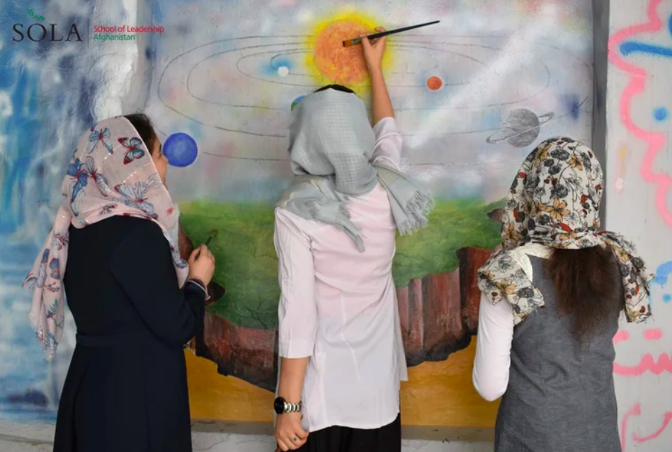  SOLA students painting a mural of Afghanistan on one of the walls at SOLA’s Kabul campus. 